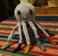 Kreative handgefertigte Strickfigur eines Oktopus mit bunten Tentakeln auf einem bunten Stoffuntergrund, ideal für handgemachte Dekorationen und kreative Bastelprojekte.