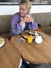 Frau beim Frühstück mit Kaffee, Saft und Gebäck, entspannt und glücklich, in einem gemütlichen Café, passend für Handmade Kultur Themen.