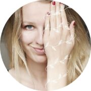 Junge Frau mit blondem Haar, die mit einer weißen, blattverzierten Schnur spielt, symbolisiert kreative Handarbeit und Kunsthandwerk bei Handmade Kultur.