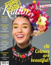 Frau mit buntem Blumenkranz und traditioneller Kleidung, die kreative Handwerkskunst und DIY-Projekte präsentiert, ideal für Handmade- und Kulturinteressierte.