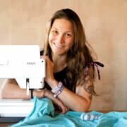 Frau beim Nähen mit Nähmaschine, kreative Handarbeit, Stoffe und Nähzubehör, Fokus auf handgemachte Textilkunst und DIY-Projekte.