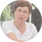 Frau mit kurzen braunen Haaren und Brille, spricht in einem Interview, umgeben von grünen Pflanzen und einem modernen Hintergrund, betont handgemachte Kultur und Kreativität.