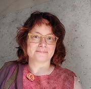 Frau mit Brille und handgemachtem Kleid, die kreative Handwerkskunst bei HANDMADE Kultur präsentiert.