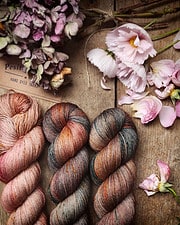 Bunte handgefärbte Wolle, umgeben von zarten Blumen und Lavendel, ideal für kreative Handarbeiten und Strickprojekte.