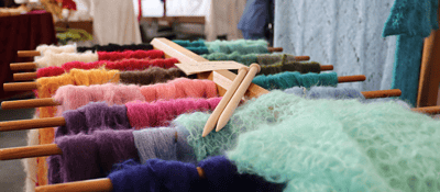 Bunte handgestrickte Wolle auf Holzdrehstangen, Farbvielfalt, kreative Strick- und Wollwaren, handmade, kreative Textilkunst, Handarbeit, Wollkunst, textiles Kunsthandwerk.