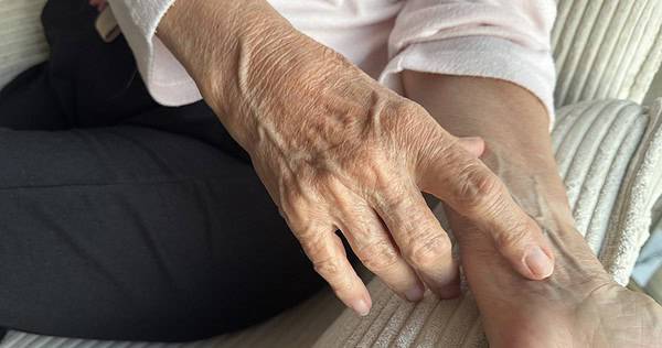 Alte Hände halten die Hand einer älteren Person, Nahaufnahme, Pflege, Unterstützung, Geborgenheit, fürsorgliche Berührung, Seniorenpflege, emotional, Begleitung, Menschlichkeit.