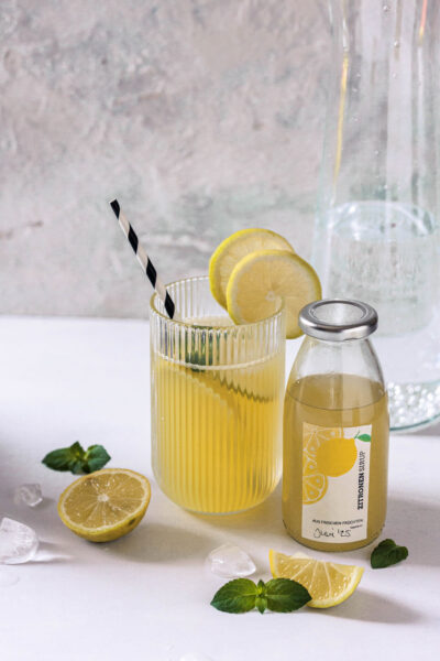 Erfrischender Zitronenlimonade mit frischen Zitronenscheiben, Zitronensorbet, handgemachte Glasflasche und Minzblätter auf weißem Hintergrund.