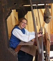 Frau beim Spinnen mit einer historischen Spinnmaschine, handgefertigte Textilien, traditionelles Handwerk, nachhaltige Herstellung, kreative Textilkunst, regionales Kunsthandwerk.