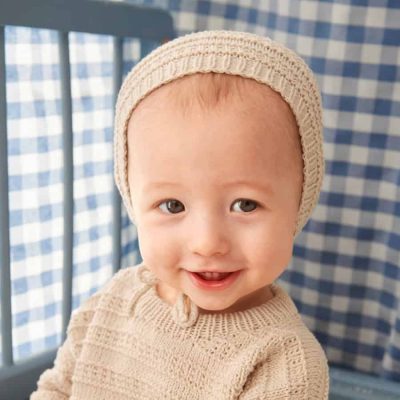 Baby mit gestrickter Fillip-Bonnet und passendem Pullover aus dem Strickset